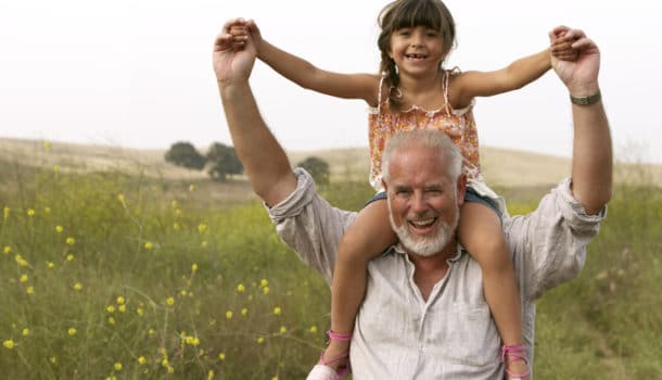 Girl (4-6) sitting on grandfather's shoulders, smiling, portrait